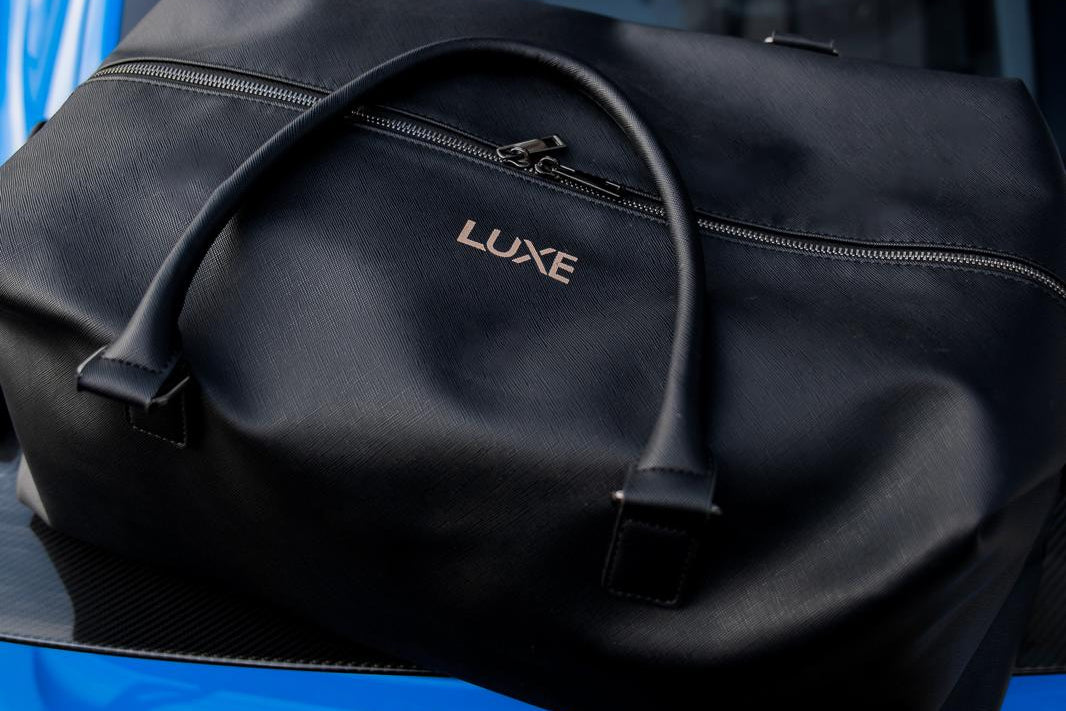 Black duffel bag labeled 'LUXE' on a blue Porsche car.